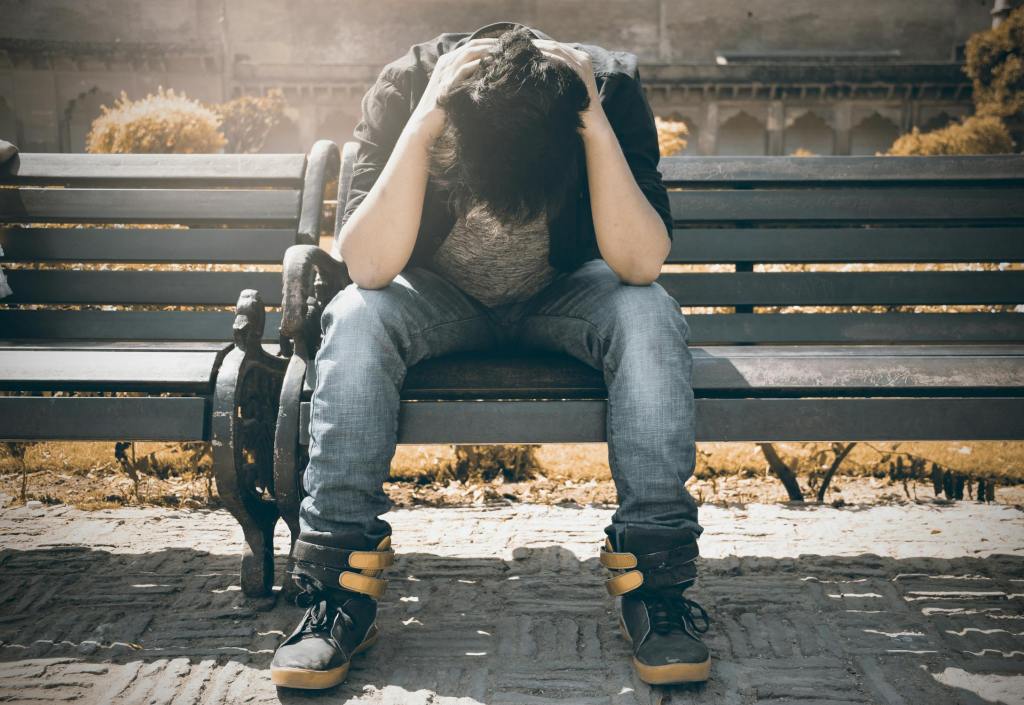 A young man sitting on a bench with his head in his hands. 